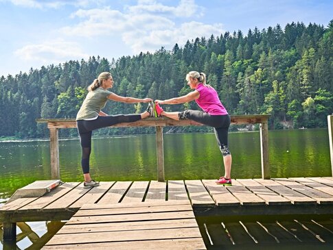 Zwei Frauen trainieren auf einem Steg am See