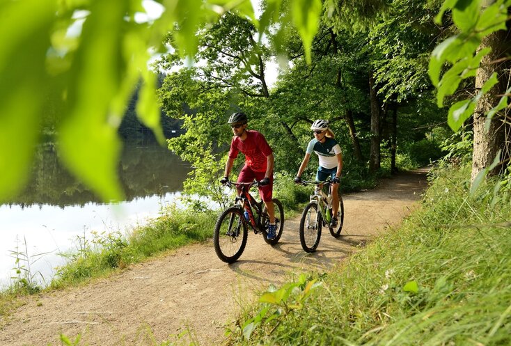 Paar fährt Fahrrad im Wald entlang eines Sees