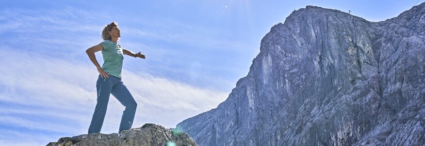 Hier sehen Sie eine Frau, die im Vordergrund eines Bergpanoramas steht. 