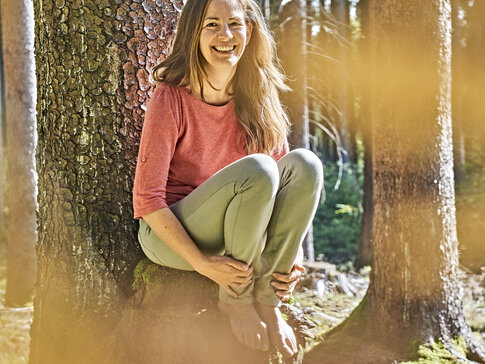 Hier sehen Sie Gesundes Bayern Expertin Nathalie Elitzer beim Waldbaden, angelehnt an einen Baum.