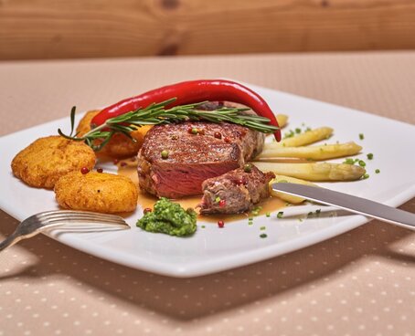 Hier sehen Sie ein Gericht auf einen weißen Teller, das aus Kartoffeln, Spargel und einem Steak besteht. 