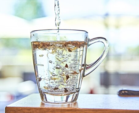 Hier sieht man eine gläserne Tasse, die mit Wasser aufgefüllt wird. 