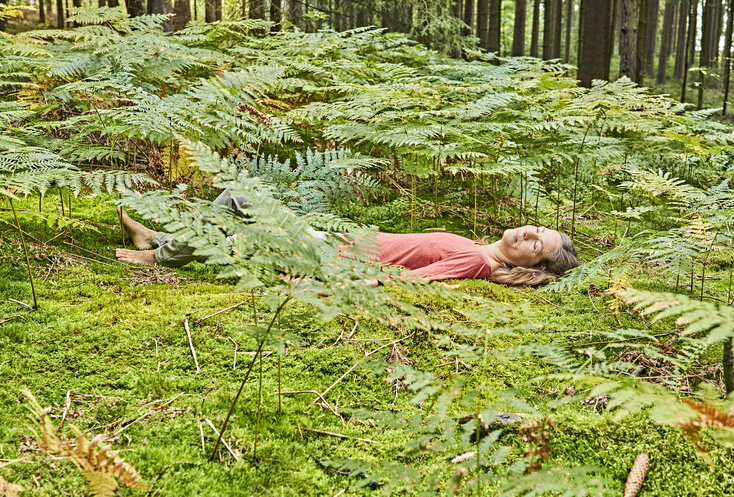 Hier sehen Sie die Gesundes Bayern Waldexpertin Nathalie Elitzer auf dem Waldboden liegen.