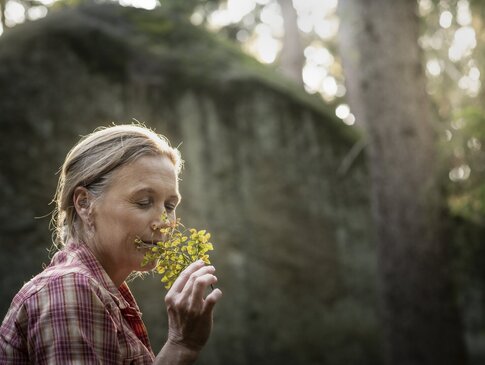 Hier sehen Sie die Bayern Botschafterin und Waldbademeisterin Elke Seidel. Sie riecht an einer Pflanze.