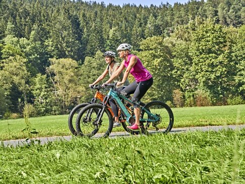 Zwei Frauen fahren gemütlich mit dem Rad durch grüne Natur 