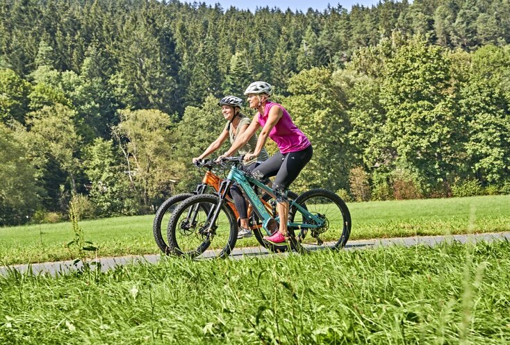 Hier sehen Sie zwei Frauen auf E-Bikes fahren.