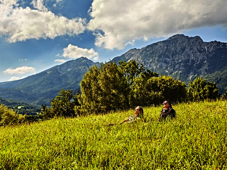 Sie sehen zwei junge Frauen in hohem Gras liegen, die Berge im Hintergrund.