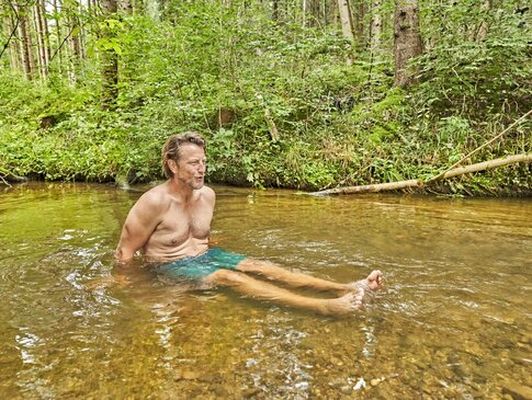 Ein Mann sitzt in Badehose in einem Bach.