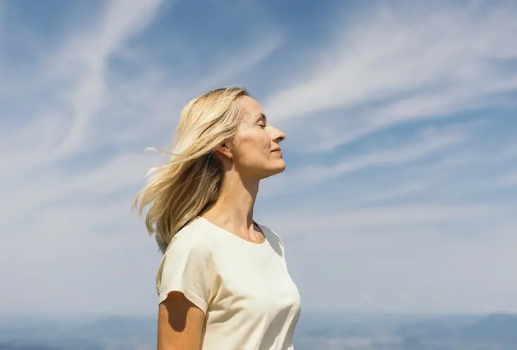 Frau mit geschlossenen Augen vor einem blauen Himmel mit Schleierwolken