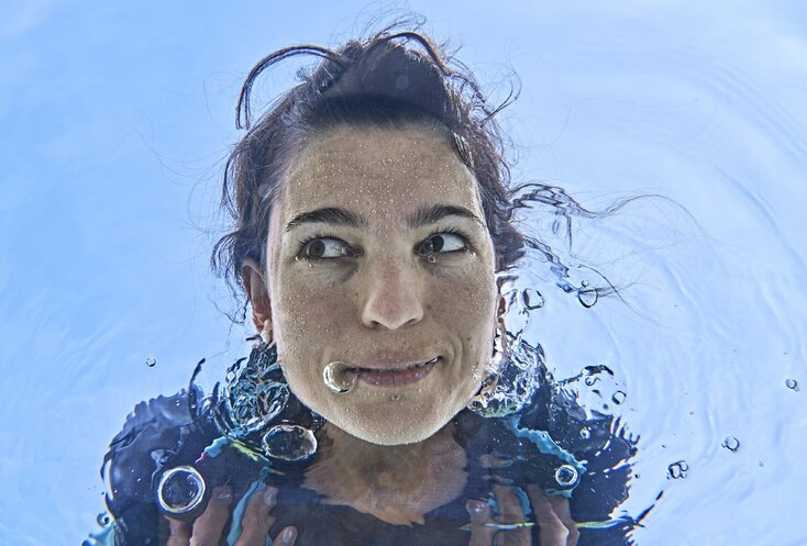 Sie sehen eine Frau die ihr Gesicht in klares Wasser taucht.