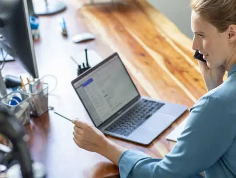 Eine Frau im Homeoffice sitzt an ihrem Schreibtisch vor ihrem Laptop und telefoniert.