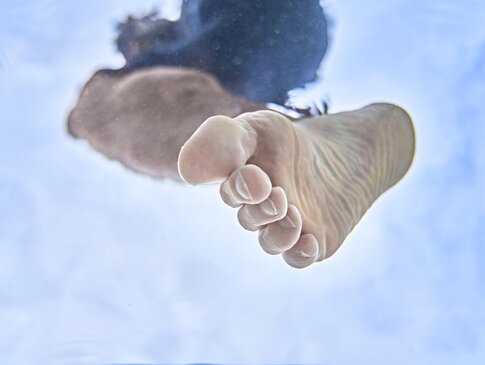 Hier sehen Sie einen Fuß, welcher in ein Wasserbecken steigt. Das Foto ist in Froschperspektive aufgenommen. Es wirkt als ob der Fuß von oben auf den Betrachter steigt.