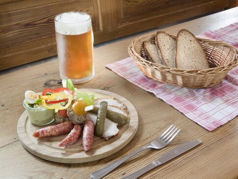 Hier sehen Sie einen Bortzeitteller mit Wurst, Bauernbrot, Käse und ein Bier.