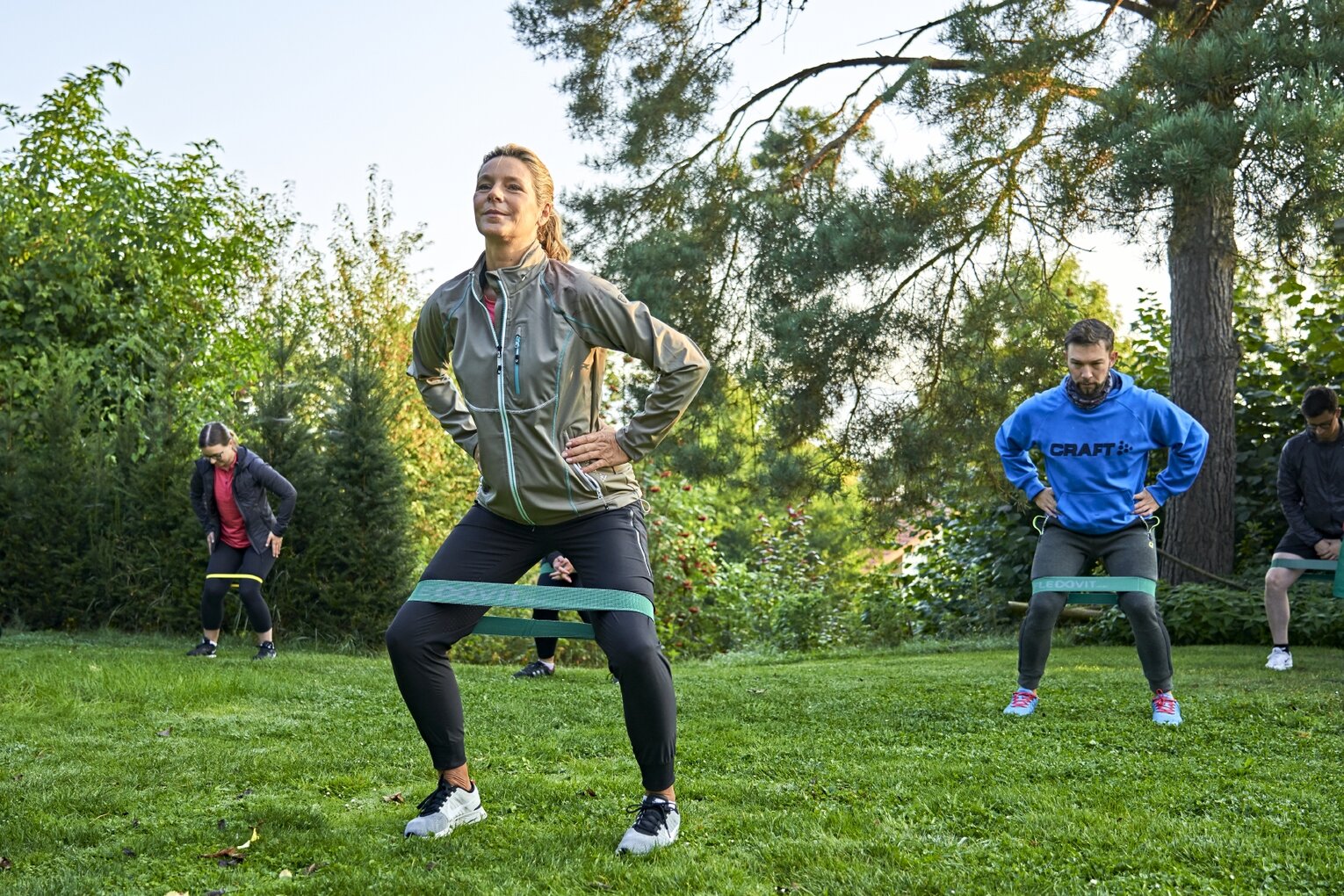 Hier sehen sie 3 Menschen beim gemeinsamen Gruppentraining mit Theraband im Garten