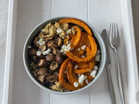 Hier sehen Sie eine Hirse Bowl mit Pilzen und Kürbis auf einem weißen holz Tablett. 