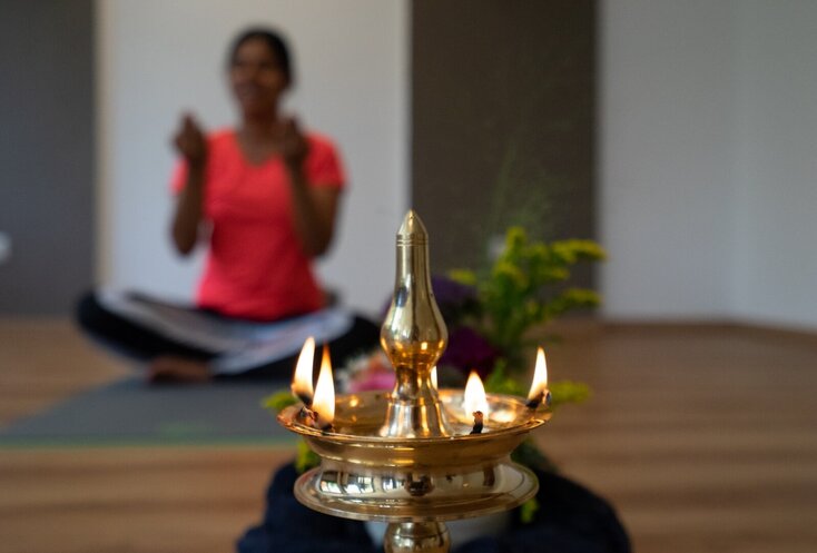 Hier sehen Sie im Hintergrund eine Frau, welche Yoga praktiziert. Im Vordergrund sehen Sie ein Räucherobjekt. 