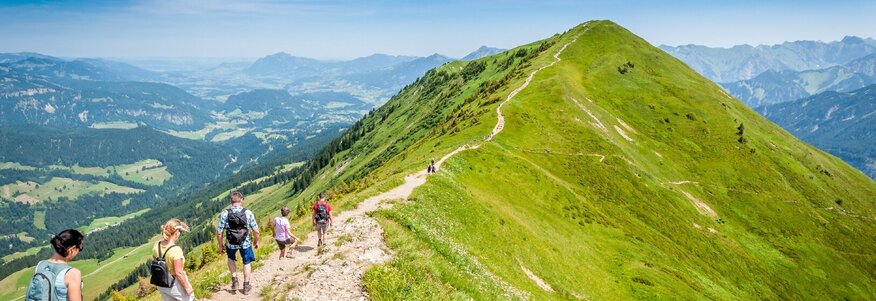 Hier sehen Sie Personen auf der Spitze eines Berges wandern. Unter ihnen liegt das Tal. 