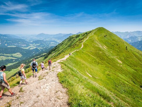 Hier sehen Sie Personen auf der Spitze eines Berges wandern. Unter ihnen liegt das Tal. 