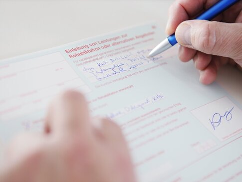 Hier sehen Sie wie eine Person ein Rezept ausfüllt. Es sind nur die Hände und der Kugelschreiber auf dem Blatt Papier zu sehen. 