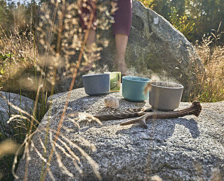 Hier sehen Sie dampfende Teetassen auf Steinblock in der Natur.