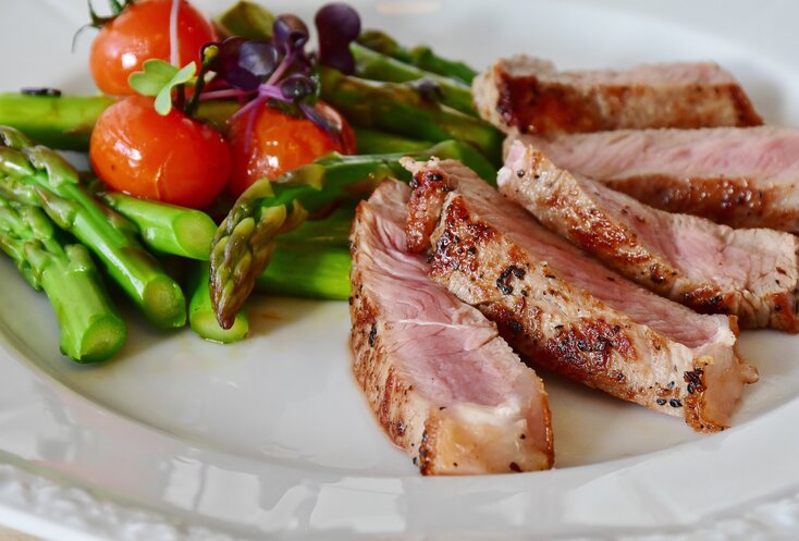 Hier sehen Sie ein Gericht auf einem weißen Teller serviert. Das Gericht besteht aus feinen scheiben Fleisch und Spargel und kleine Cocktailtomaten