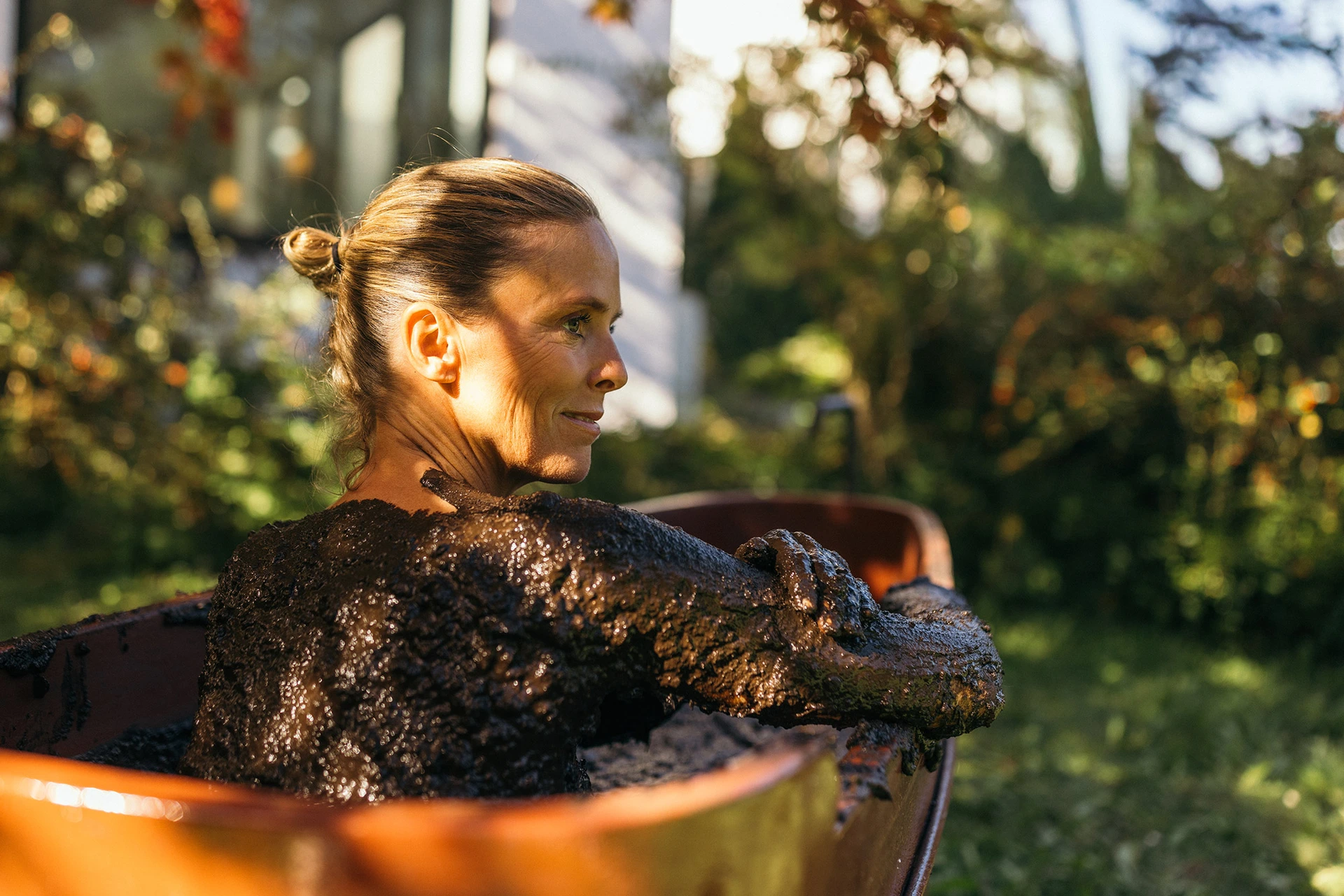 Frau sitzt in einer hölzernen Badewanne bei einer Moorkur