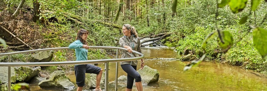 Hier sehen Sie zwei Frauen, die durch einen knöchelhohen Bach waten.