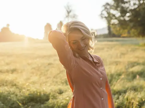 Frau steht auf einer Wiese im Sonnenlicht der Abendsonne