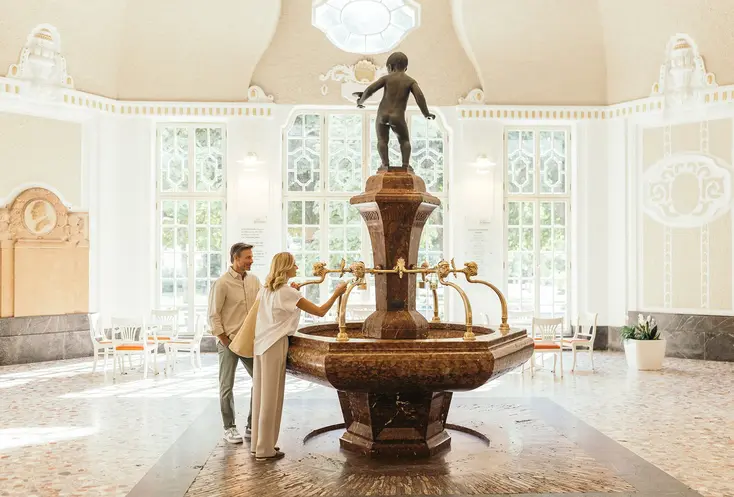 Ein Paar an einem Heilwasser-Trinkbrunnen im bayerischen Staatsbad Bad Kissingen