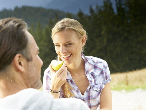Hier sehen Sie eine Frau und einen Mann in den Bergen. Die Frau isst einen Apfel.