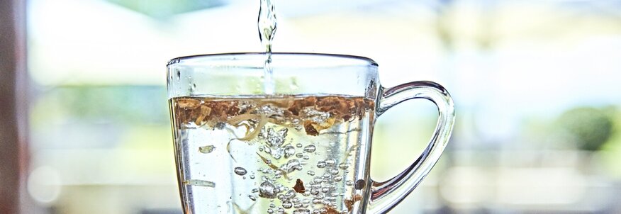 Hier sieht man eine gläserne Tasse, die mit Wasser aufgefüllt wird. 