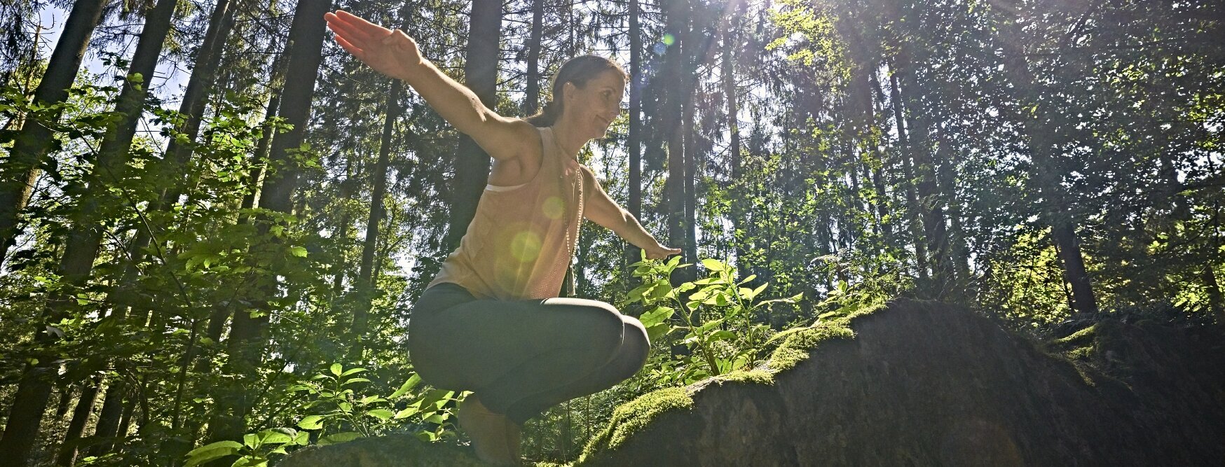 Sie sehen einen jungen Mann in der Hocke mit ausgestreckten Armen im Wald.