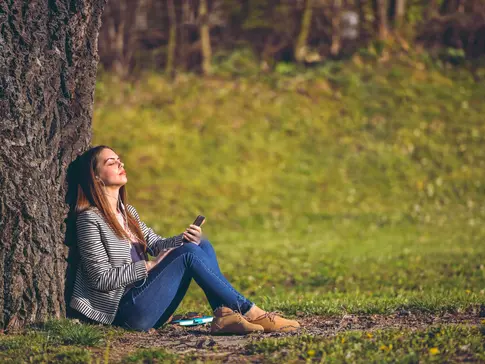 Frau hört Musik und lehnt am Baum