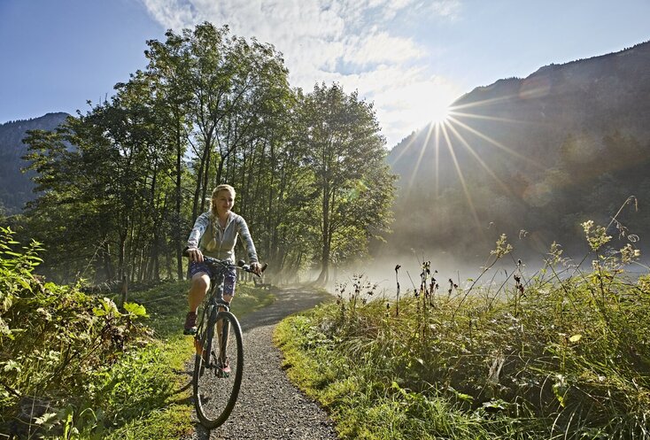 Hier sehen Sie eine junge Frau, die mit dem Fahrrad durch üppig grüne Wiesen und Wälder fährt.