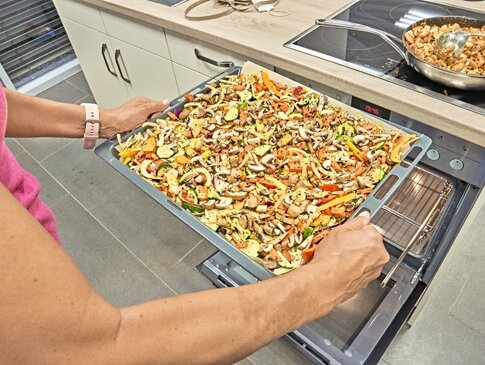 Hier sehen Sie eine Person, welche ein Blech mit Gemüse in den Ofen schiebt.