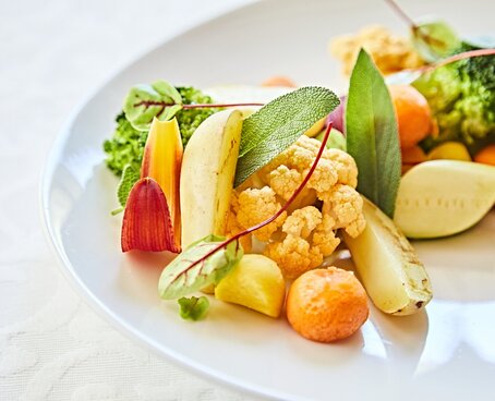 Hier sehen Sie ein Gericht auf einem Teller angerichtet. Zu sehen ist ein Stück Gemüselasagne sowie Gedünstetes Gemüse, wie Brokkoli, Blumenkohl und Karotte. 