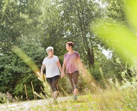 Hier sehen Sie zwei Frauen, welche durch eine Kurpark spazieren gehen und sich miteinander unterhalten. 