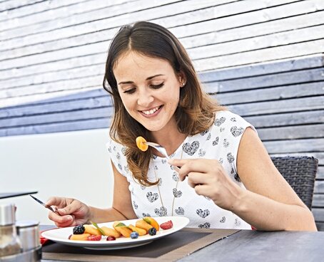 Hier sehen Sie eine junge Frau, die lächelnd gekochtes Obst und Gemüse isst.