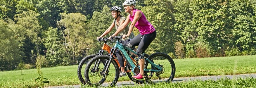 Hier sehen Sie zwei Frauen auf E-Bikes fahren.