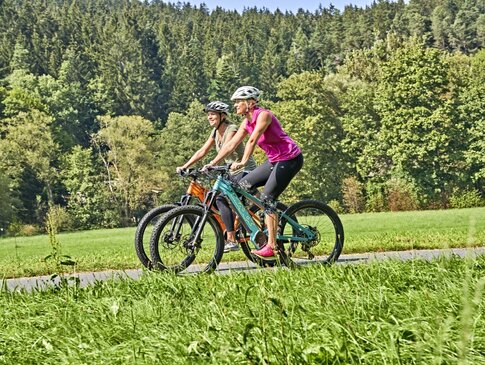 Hier sehen Sie zwei Frauen auf E-Bikes fahren.