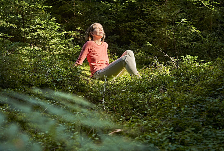 Hier sehen Sie Gesundes Bayern Waldexpertin Nathalie Elitzer beim Waldbaden mit Sonnenschein im Gesicht.