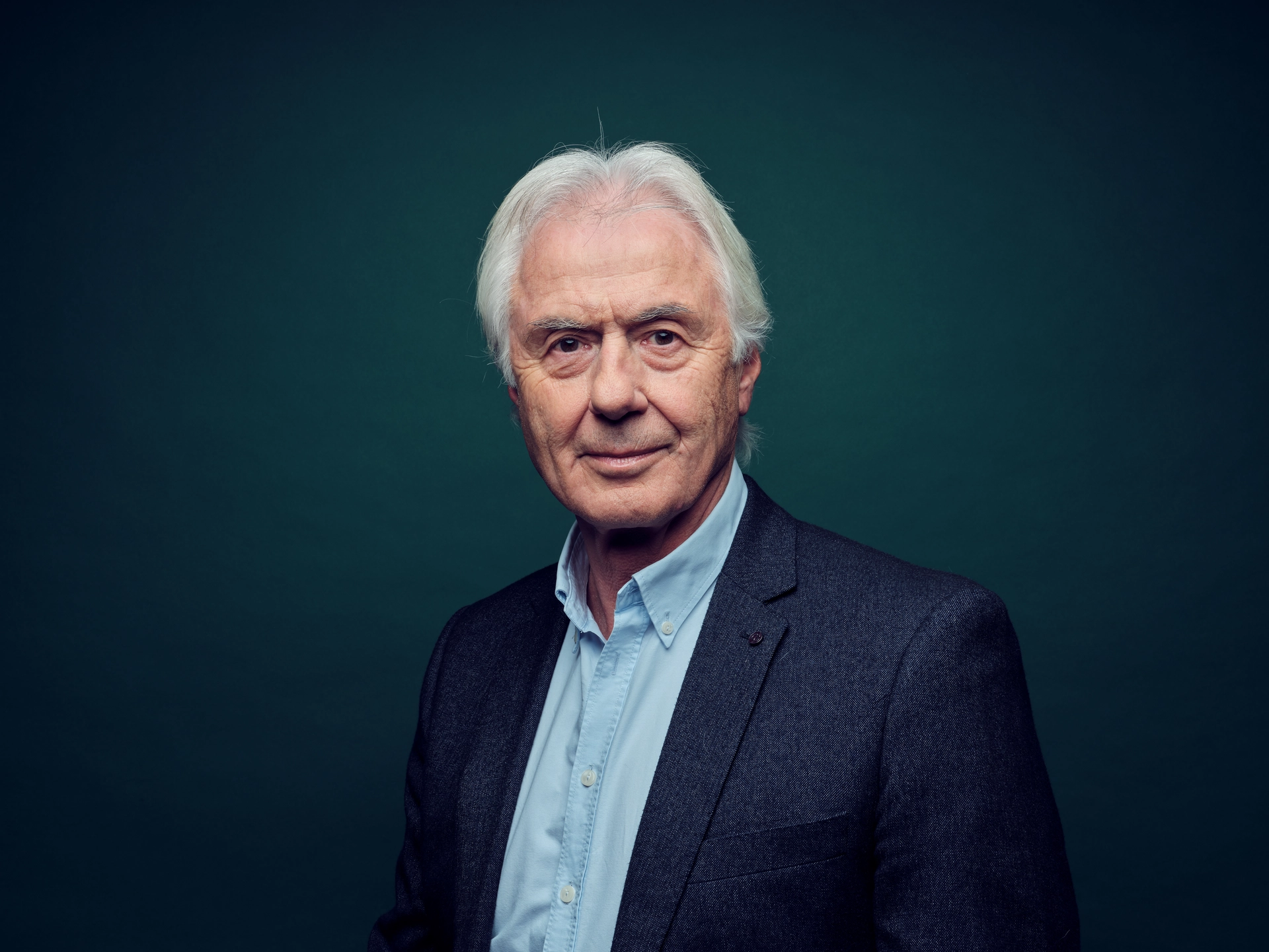 Hier sehen Sie den #gesundkannjeder Experten Wolfgang Sommerfeld. Er trägt ein hellblaues Hemd und einen dunkelblauen Sakko. Der Hintergrund ist einfarbig un dunkel. 
