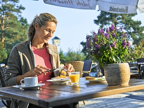 Hier sehen Sie eine Frau auf einer Hotelterrasse frühstücken.