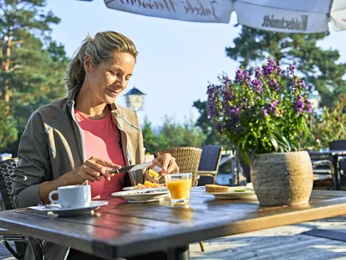 Hier sehen Sie eine Frau auf einer Hotelterrasse frühstücken.