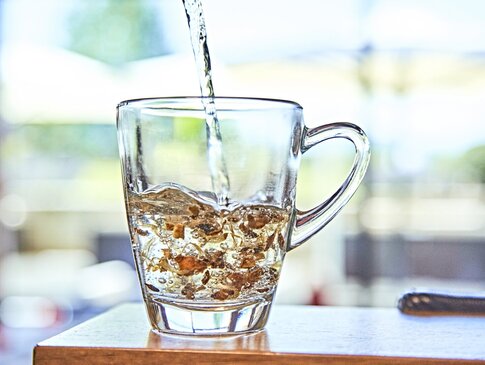 Hier sehen Sie eine Tasse aus Glas mit getrockneten Kräutern. Es wird Wasser aufgegossen. 