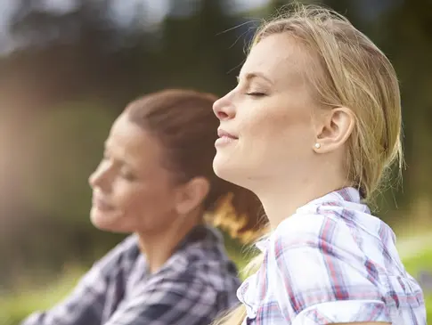 Nahaufnahme von zwei Frauen, die in einer Wiese sitzen und tief durchatmen.