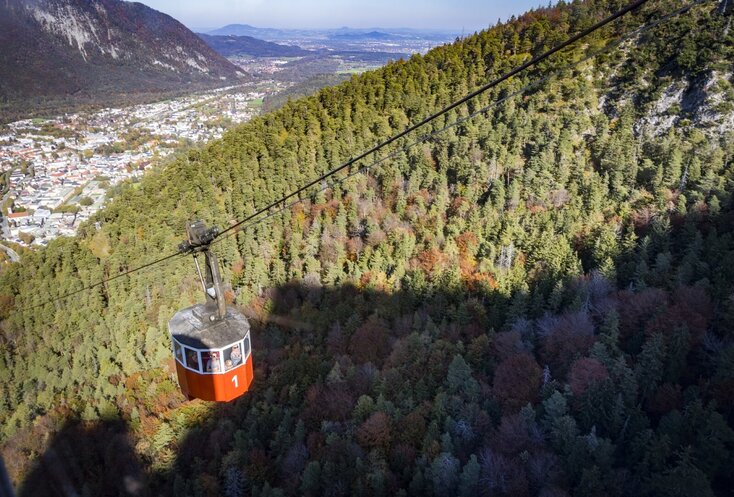 Die kleine rote Gondel der Predigtstuhlbahn bringt die Gäste auf den Berg. Darunter ist am Berghang ein dichter Wald zu sehen und die Gebäude der Stadt Bad Reichenhall.