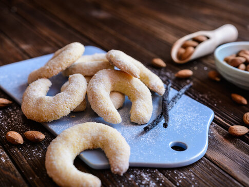 Hier sehen Sie weihnachtliche Vanillekipferl. Diese wurden mit Mandelmelh zubereitet. Neben den Vanillekipferl sind Mandeln in einer Schüssel.