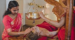 Zwei indische Therapeuten führen einen ayurvedischen Stirnguss durch